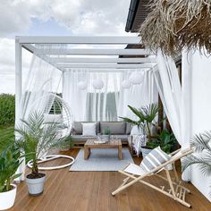 an outdoor living area with white curtains and plants on the deck, surrounded by greenery