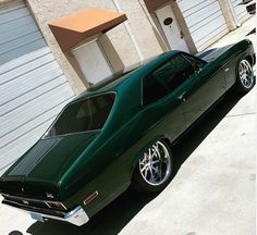 a green muscle car parked in front of a garage