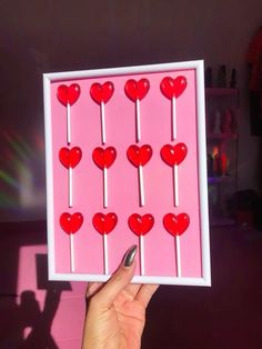 a person holding up a pink card with red hearts on it in front of a purple background