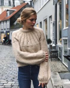 a woman is standing on the street with her hand in her pocket and wearing a sweater