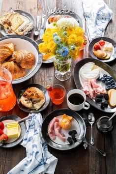 a wooden table topped with plates and bowls filled with different types of breakfast foods on top of it