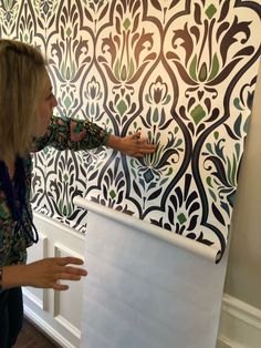 a woman is painting a wall with black and white designs on the wall behind her