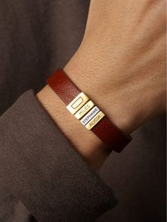 a man wearing a red leather bracelet with two gold bars on it's wrist