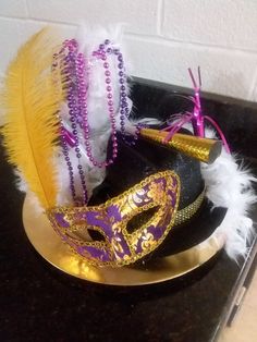 two mardi gras masks are sitting on a black plate with gold and purple feathers