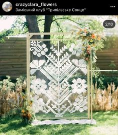 a white and black quilt on display in the grass next to a fence with flowers