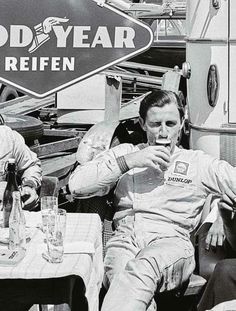 two men sitting at an outdoor table eating food and drinking beverages in front of a good year sign