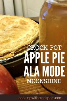 an apple pie sitting on top of a wooden table next to a jar of liquid