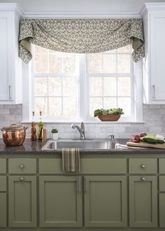 a kitchen with green cabinets and a window above the sink that has a potted plant on it