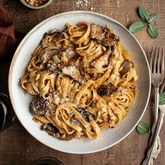 a plate of pasta with meat and mushrooms on it next to two glasses of wine