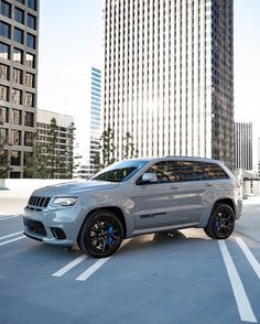 a silver jeep parked in the middle of a parking lot with tall buildings behind it