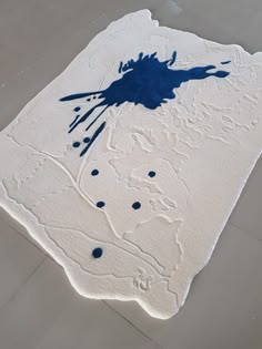 a white rug with blue paint splattered on it in the middle of a floor