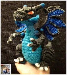 a crocheted blue and black dragon sitting on top of a person's hand