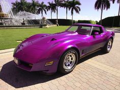 a purple sports car parked on the side of a road next to palm trees and water