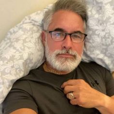 an older man with glasses pointing to the side while laying in bed on his stomach