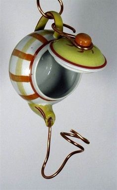 a teapot hanging from a hook on a white wall with an orange and yellow stripe design