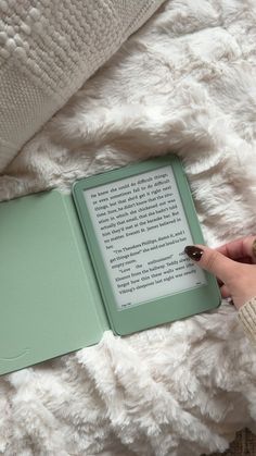 a person is reading a book on a bed with white blankets and a green cover