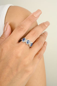 a woman's hand with three blue stones on her left and the other hand holding an engagement ring