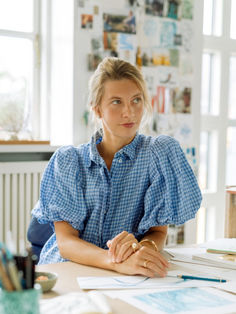 a woman sitting at a table with papers and pens in front of her, looking off to the side