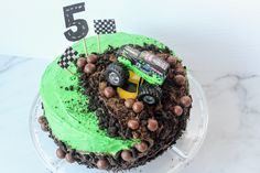 a birthday cake with green frosting and monster trucks on top is decorated with dirt