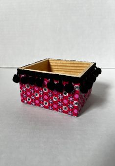 a pink and black box with pom poms on the top sitting on a white surface