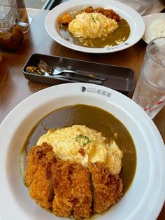 two white plates with food on them sitting on a table next to glasses and utensils