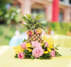 a pineapple with sunglasses on top of it sitting on a table surrounded by flowers