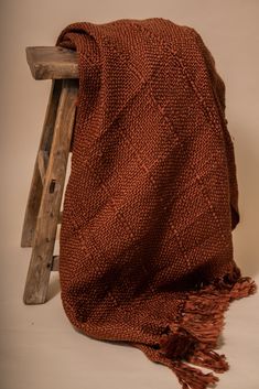 an orange blanket sitting on top of a wooden chair next to a ladder with a piece of wood sticking out of it