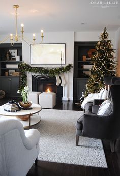 the living room is decorated for christmas with white furniture and black bookshelves, stockings, garlands, candles, and a fireplace