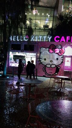 a hello kitty cafe is lit up at night with people walking around the outside area