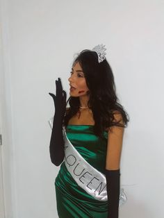 a woman in a green dress and black gloves holding her hand up to the side