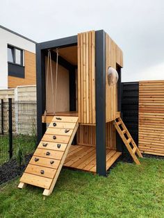 a small wooden structure with steps leading up to the top and bottom floor, in front of a fenced yard