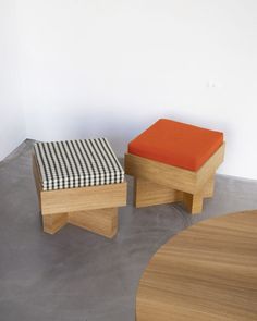 two wooden stools sitting next to each other on top of a cement floor in front of a white wall