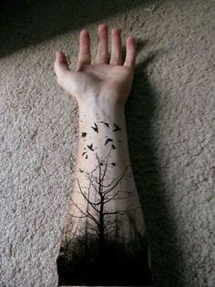 a person's arm with a tree and birds on it, in front of a wall