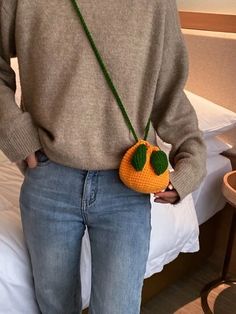 a woman is holding a crocheted orange purse in her hand while standing on a bed