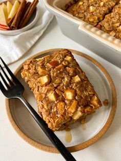 a white plate topped with granola next to a bowl of apples and a fork