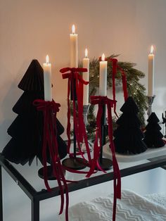 some candles are sitting on a table with red ribbon around them and black trees in the background