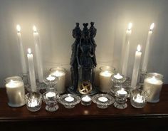 there are many candles on the table with one candle in front of it and two statues behind them