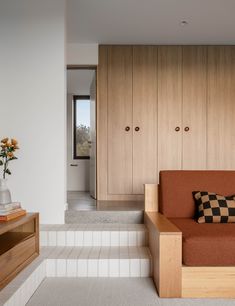 a brown couch sitting on top of a white floor next to a wooden shelf filled with vases