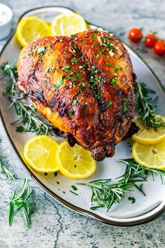 a whole chicken on a plate with lemons and herbs