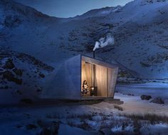 a person sitting in the window of a small cabin on top of a snow covered mountain