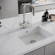 a white kitchen with marble counter tops and stainless steel faucet in the center