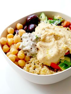 a white bowl filled with vegetables and hummus next to chickpeas on top of couscous