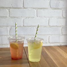 two drinks are sitting next to each other on a wooden table in front of a brick wall