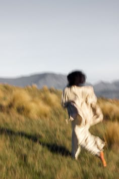 a woman running through a field with a frisbee in her hand and mountains in the background