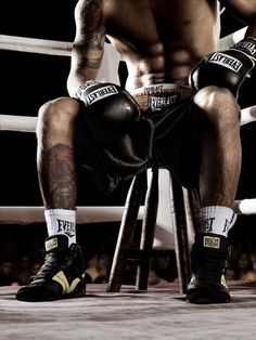 a man sitting on top of a stool next to a boxing ring wearing black gloves