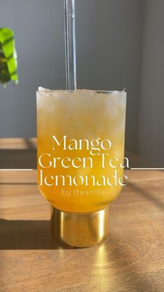 a glass filled with lemonade sitting on top of a wooden table next to a plant