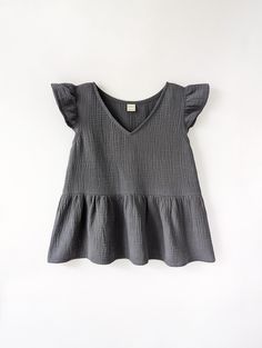 a gray top with ruffles on the shoulders and neckline is hanging up against a white wall