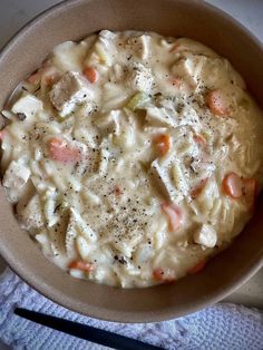 a bowl filled with macaroni and carrots on top of a table next to a fork