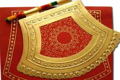 a red and gold card with some crayons on it's edge next to a pencil