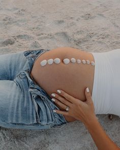 a pregnant woman laying on the beach with her belly covered in white stones and nails